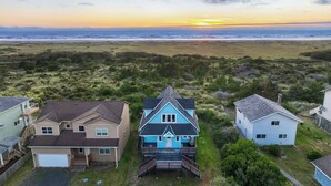 Un quartier résidentiel en bord de mer où les maisons présentent un mélange de styles architecturaux, notamment une maison bleue remarquable avec un porche et une maison beige avec un garage.
