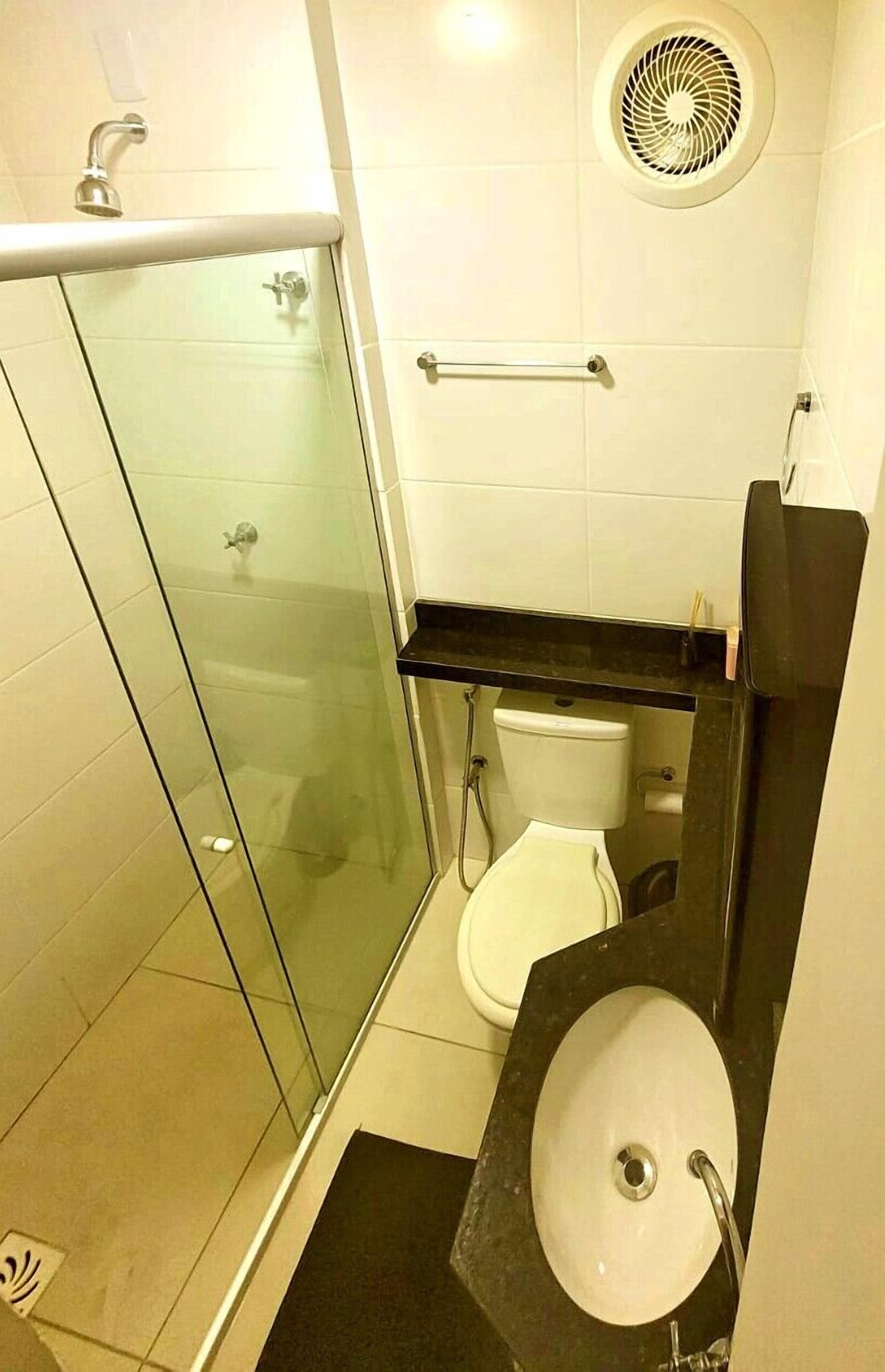 Une salle de bain moderne avec une douche à l’italienne en verre, des toilettes blanches et un lavabo sur un plan de travail noir.