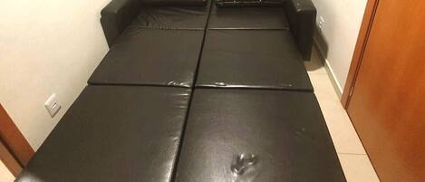 A black leather sofa with a central indentation, a small scratch on the front, and a wooden door in the background.