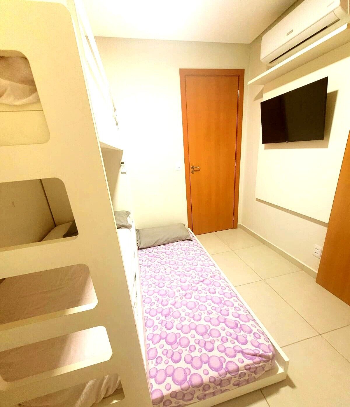 A room with a bunk bed, a door, a television, and an air conditioning unit.