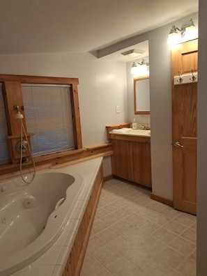 A bathroom with a bathtub, wooden vanity, and a large mirror. - Lake Iroquois.  Lakeside Retreat, Close to Williston, Burlington, Skiing (Hinesburg)