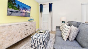 Una sala de estar con un sofá, un reposapiés y un cuadro de una playa.