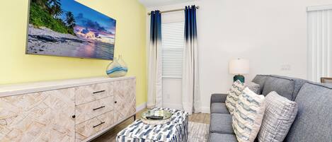 A living room with a sofa, ottoman, and a painting of a beach scene.
