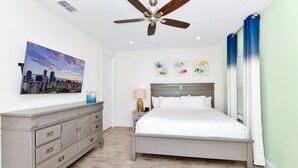 Ein Schlafzimmer mit Bett, Nachttisch, Kommode, Deckenventilator und Kunstwerken an den Wänden.