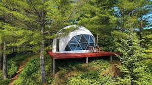 A geodesic dome structure with a red platform and wooden chairs, surrounded by dense forest. - Private Pond Retreat with Dome, Dockside Hot Tub and 3 Sleeping Spaces (Glenfield)