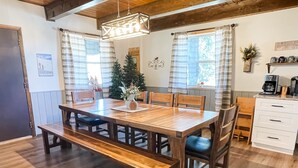 A dining area with a wooden table and benches, a chandelier, a Christmas tree, and a kitchen area with a coffee maker. - Perfect Family Cabin! 3 Master Suites, Sleeps 10, next to the park! (South Fork)