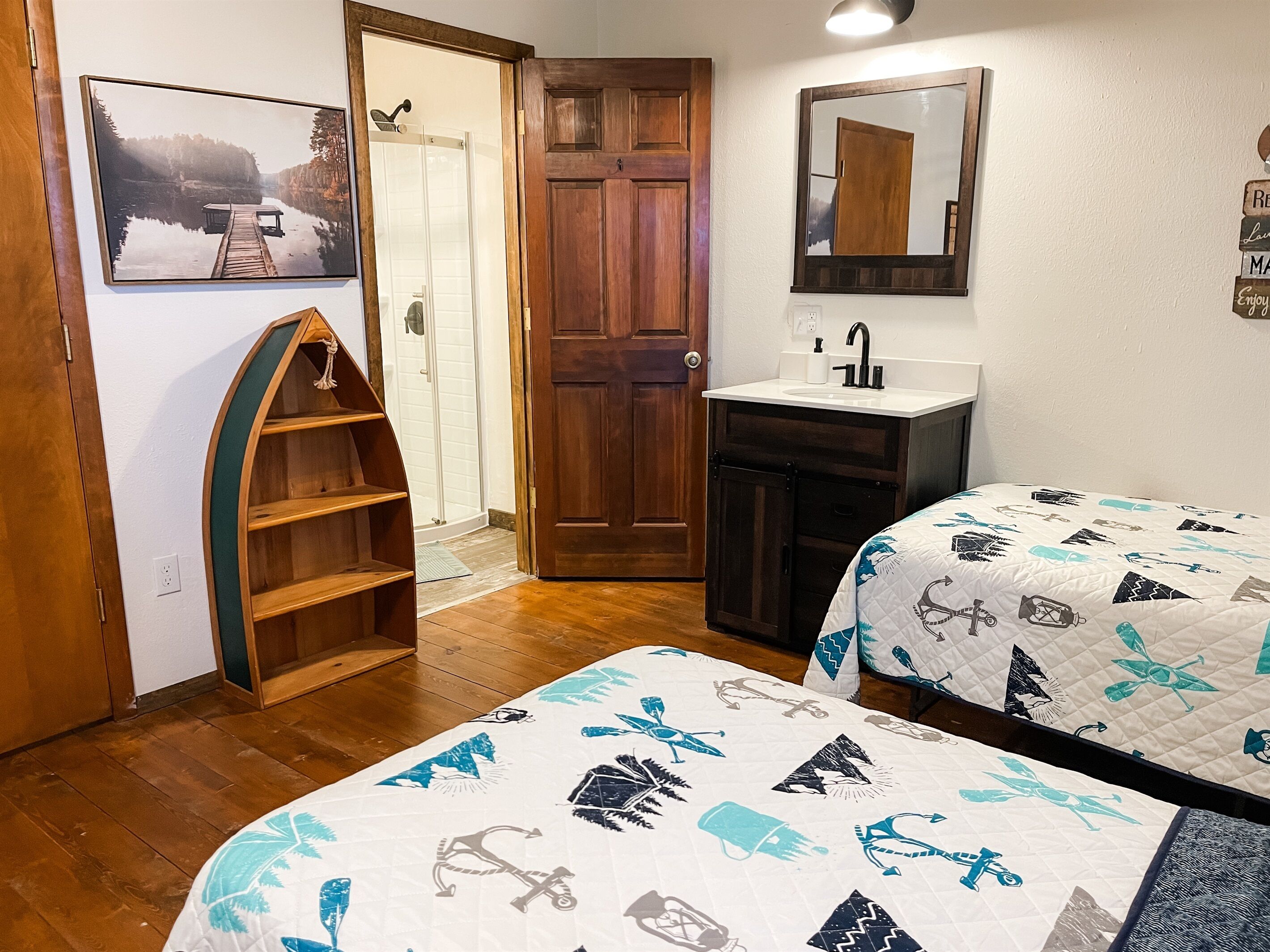 A bedroom with two beds, a wooden door, a bathroom with a sink, and a framed picture on the wall.