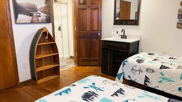 A bedroom with two beds, a wooden door, a bathroom with a sink, and a framed picture on the wall.