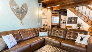 A brown leather sectional sofa with a matching ottoman, two decorative pillows, and a wall-mounted light fixture. - Perfect Family Cabin! 3 Master Suites, Sleeps 10, next to the park! (South Fork)