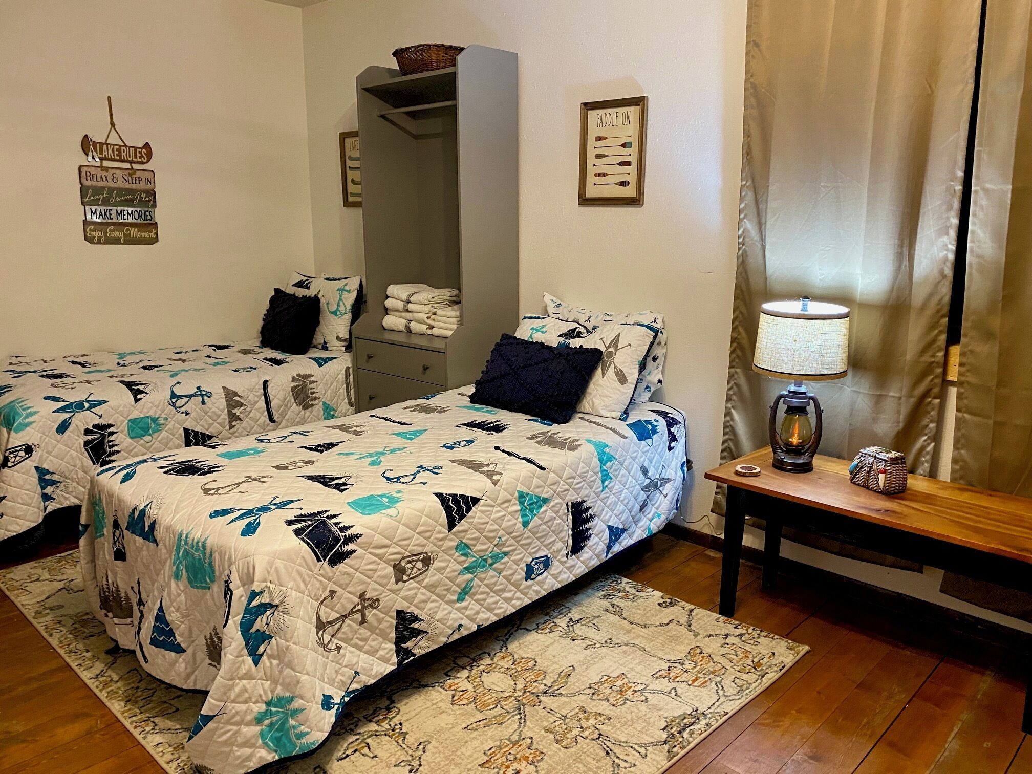 A bedroom with two beds, a nightstand, a lamp, and a framed sign on the wall.