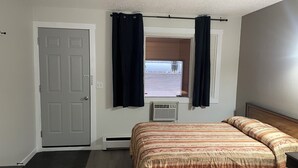 A bedroom with a bed, a window with curtains, a door, and a radiator. - Niton Junction Motel (Niton Junction)