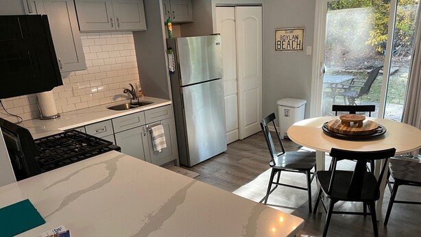 Una cocina moderna con armarios blancos, un refrigerador de acero inoxidable y un comedor con una mesa redonda y sillas.