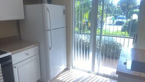 A kitchen with a refrigerator, cabinets, and a sliding glass door leading to a balcony. - Chic 2-bedroom condo with AC, WiFi in Naples, Resort like pool. 3 miles to beach (Naples)