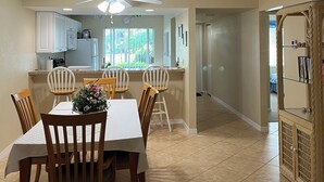 A dining area with a table set for four, a kitchen in the background, and a hallway leading to another room. - Chic 2-bedroom condo with AC, WiFi in Naples, Resort like pool. 3 miles to beach (Naples)