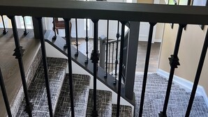 Un escalier avec une rampe noire menant à un palier agrémenté d’un lustre et de plantes en pot.