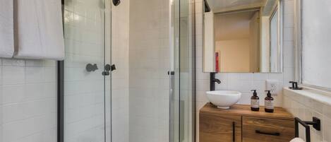 A modern bathroom with a glass-enclosed shower, a white sink, wooden vanity, and a large mirror.