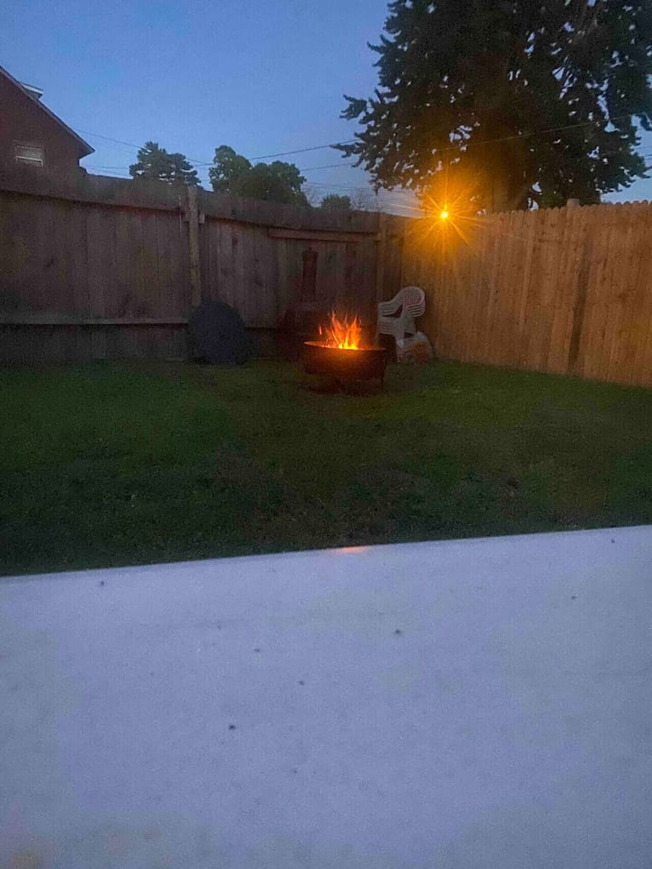 A backyard with a fire pit, a wooden fence, and a tree.