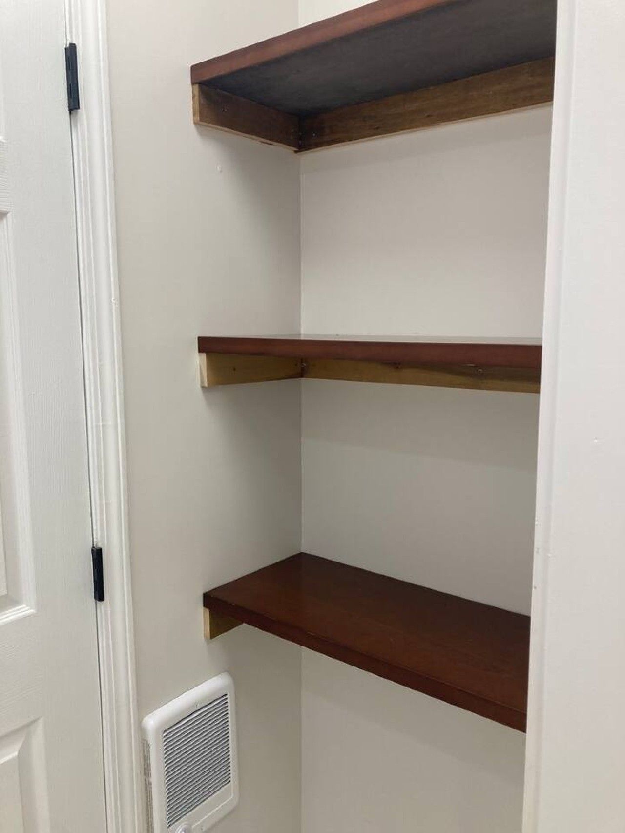 A corner of a room with white walls and three wooden shelves.