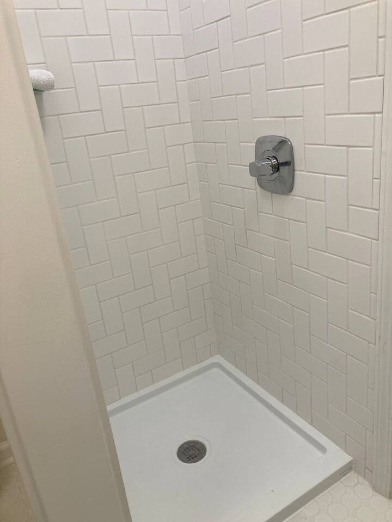 A shower with white tiled walls and a metal shower control.