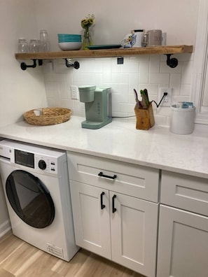 A kitchen with a washing machine, a coffee maker, and a shelf with various items. - Chic Studio in Downtown Danville Centre, pets OK (Danville)