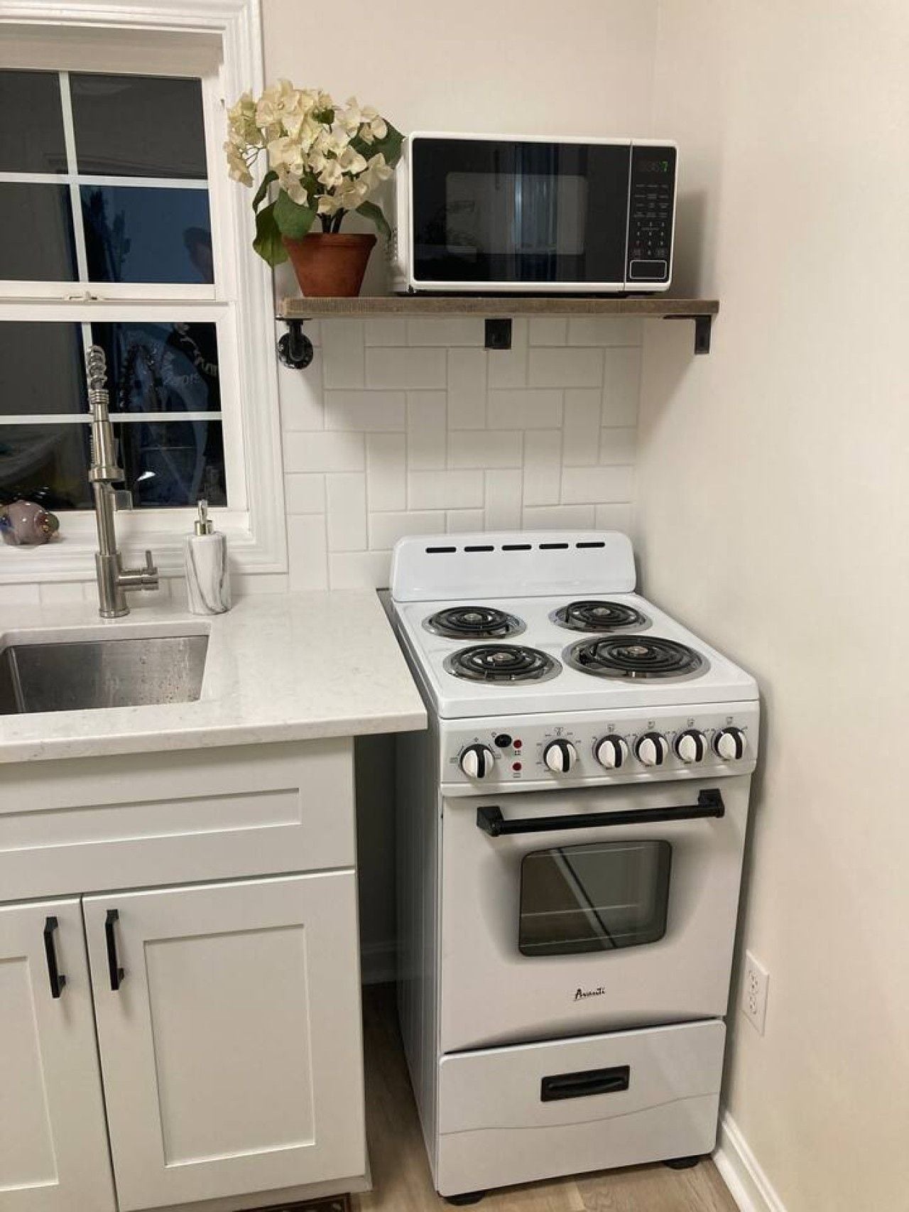 Une cuisine avec un four blanc, un four à micro-ondes placé au-dessus, et une plante en pot sur le plan de travail.