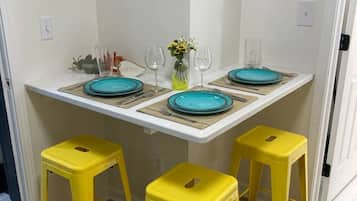 Un comedor con una mesa blanca preparada para cuatro personas, taburetes amarillos y un jarrón con flores.