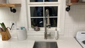 A kitchen with a stainless steel sink, white cabinets, a window with a view, and a potted plant on the counter. - Chic luxury studio, Downtown Danville, Pets OK, Centre College & Bourbon Trail  (Danville)