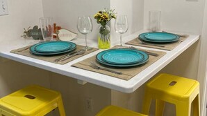 Une table à manger avec des assiettes bleues, des tabourets jaunes et un vase rempli de fleurs jaunes.