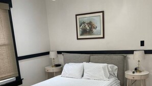 Une chambre à coucher avec un grand lit, deux tables de chevet, un tableau accroché au mur et un luminaire au plafond.