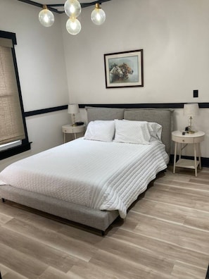 A bedroom with a large bed, two bedside tables, a wall-mounted picture, and a ceiling light fixture. - Chic Studio in Downtown Danville Centre, pets OK (Danville)