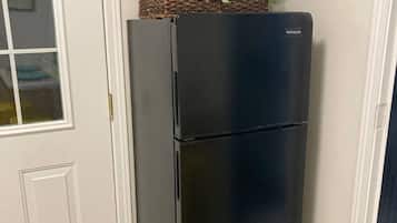 Un refrigerador negro con una cesta y plantas encima, ubicado frente a una puerta y pared blancos.