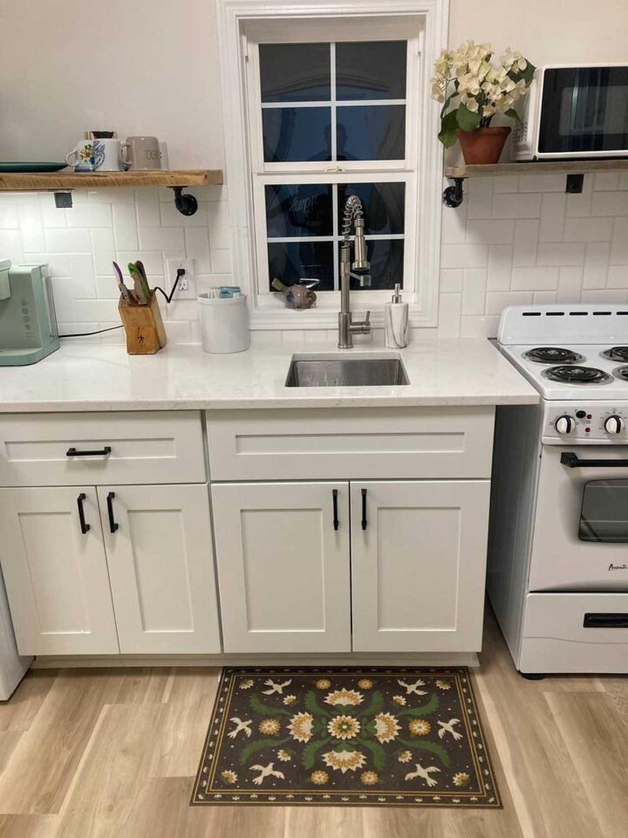 A kitchen with white cabinets, a stainless steel sink, a stove, and a window above the sink.