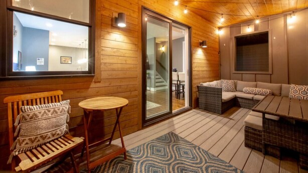 Un intérieur chaleureux, avec des éléments en bois, comprenant un canapé, une petite table et un banc. Une porte vitrée donne accès à un espace cuisine.