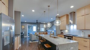 Une cuisine moderne dotée d’un îlot en marbre, d’appareils électroménagers en acier inoxydable et de luminaires suspendus.