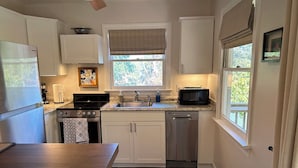 A compact kitchen with white cabinets, a stainless steel dishwasher, a gas stove, and a microwave. - Charming studio in lovely Topping with AC, WiFi that has stunning water views! (Topping)