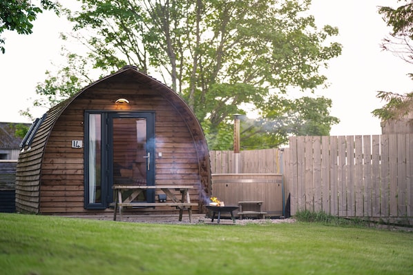 Une cabane en bois avec une porte, une table de patio et un barbecue.