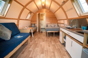 A compact, wooden interior with a kitchenette, a sofa, and a bed. - Cosy Rural Cabin With Accessible Facilities (Kinloss)