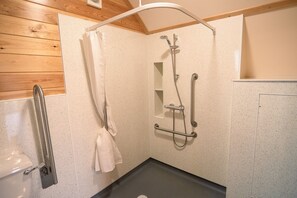A shower area with a handheld showerhead, a grab bar, and a white towel hanging on a rack. - Cosy Rural Cabin With Accessible Facilities (Kinloss)