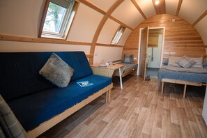A cozy, compact room with a curved ceiling, a sofa, a small table with glasses, and a bed. - Cosy Rural Cabin With Accessible Facilities (Kinloss)