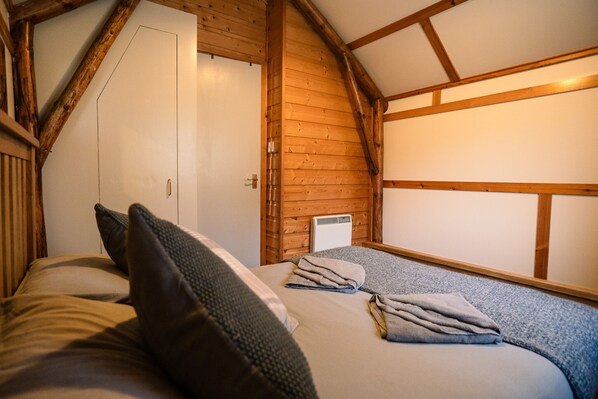 A bedroom with wooden beams, a bed with pillows and a folded blanket, and a white door. - Rustic Log Cabin With Hot Tub (Kinloss)