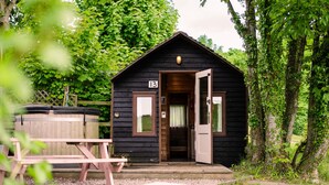 A small, dark wooden cabin with a number 13 sign, a wooden bench, and a hot tub in the foreground. - Rustic Log Cabin With Hot Tub (Kinloss)