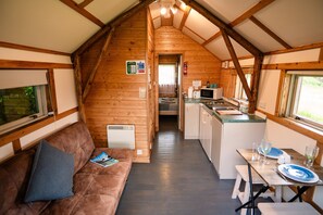 A cozy cabin interior with a wooden ceiling, a sofa with a pillow, a dining table set with plates and glasses, and a kitchen area with a microwave. - Rustic Log Cabin With Hot Tub (Kinloss)