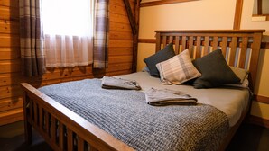 A wooden bed with a headboard, a window with curtains, and a bedspread. - Rustic Log Cabin With Hot Tub (Kinloss)