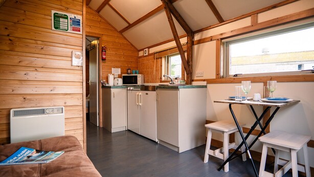A cozy cabin interior with a kitchenette, a dining area, and a living space with a couch. - Rustic Log Cabin With Hot Tub (Kinloss)