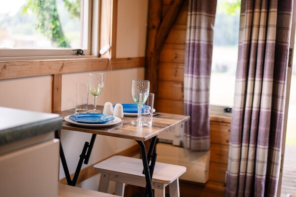 A wooden table with a blue plate, two glasses, and salt and pepper shakers in a room with wooden walls and a window.