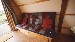 A wooden bench with a quilted backrest and cushions, positioned in a room with wooden beams and a wooden floor.