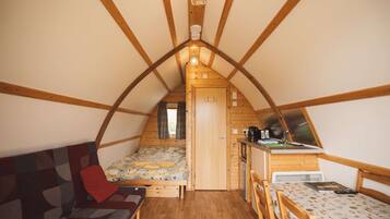 A cozy attic bedroom with a bed, a sofa, a small kitchenette, and a window.