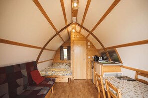 A cozy attic bedroom with a bed, a sofa, a small kitchenette, and a window. - Romantic Cosy Glamping Cabin With Luv Tub (Llanbrynmair)