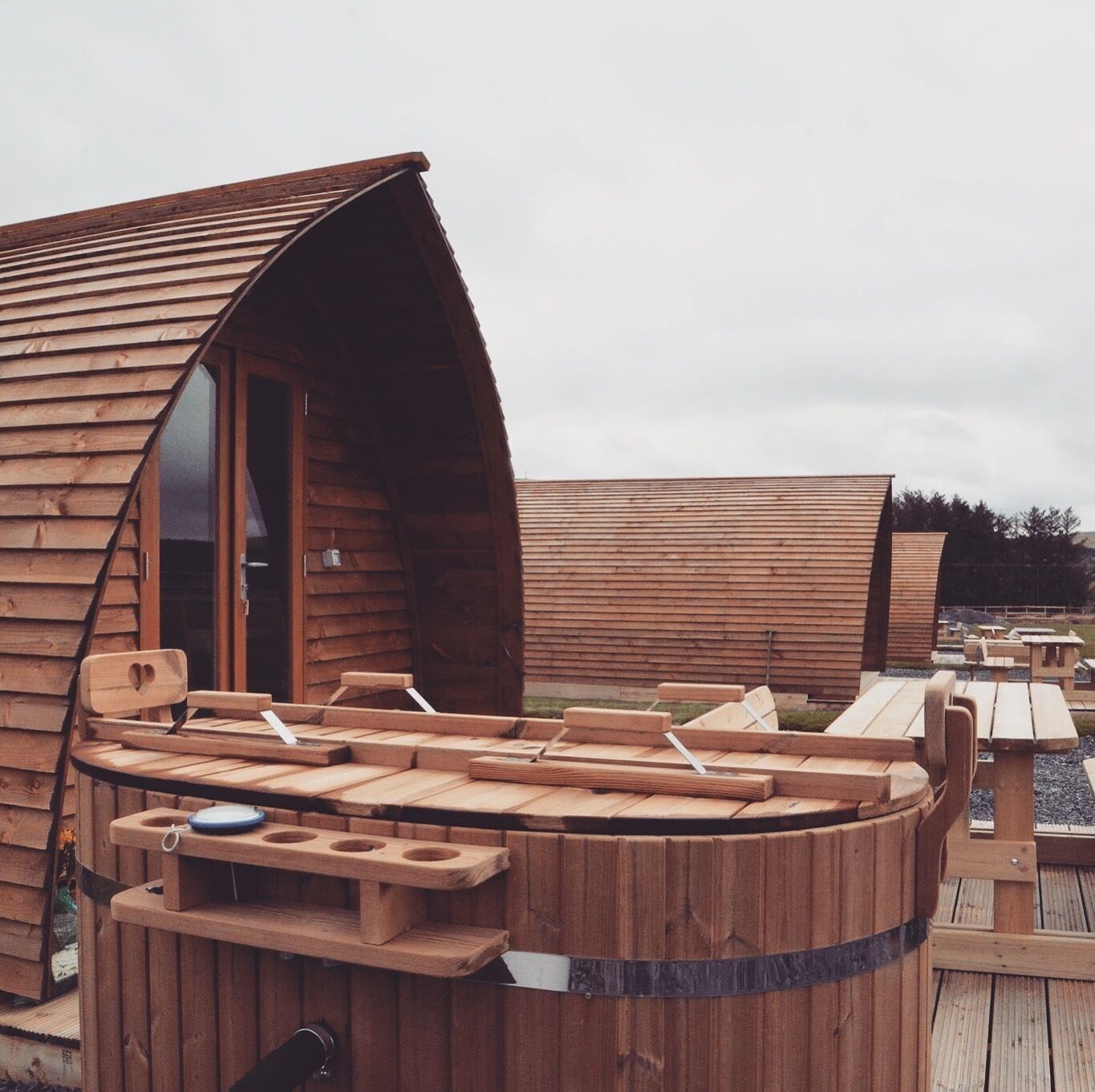 Eine Holzhütte mit gewölbter Dachform und einem runden Holztisch mit Bänken.