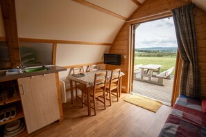 A cozy cabin with a dining area, a TV, and a view of the outdoors. - Cosy Cabin with Hot Tub in the Welsh Countryside (Llanbrynmair)